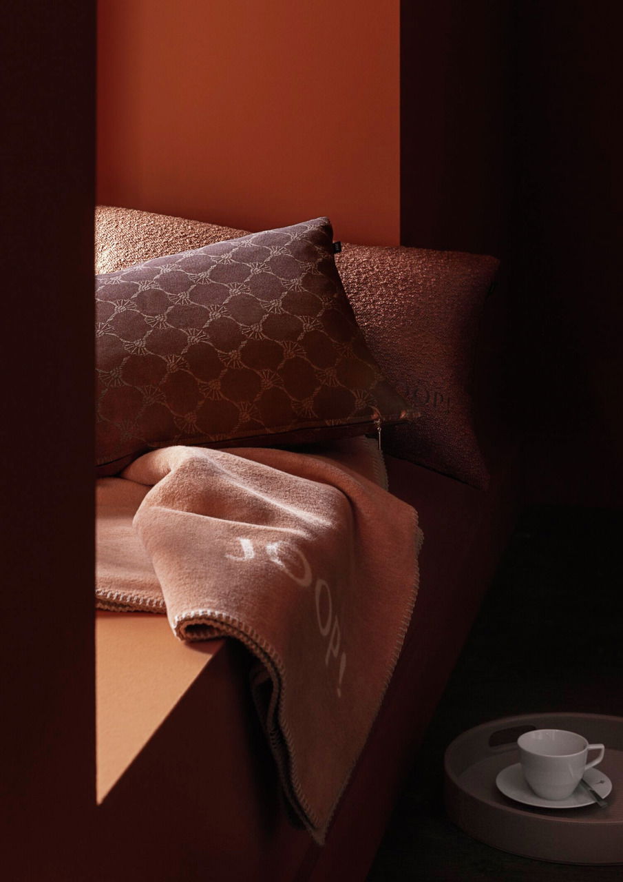 Gemütliche braune Decke und Kissen auf einem Sofa, mit einer Tasse auf einem Tablett im Vordergrund, seitliche Perspektive.