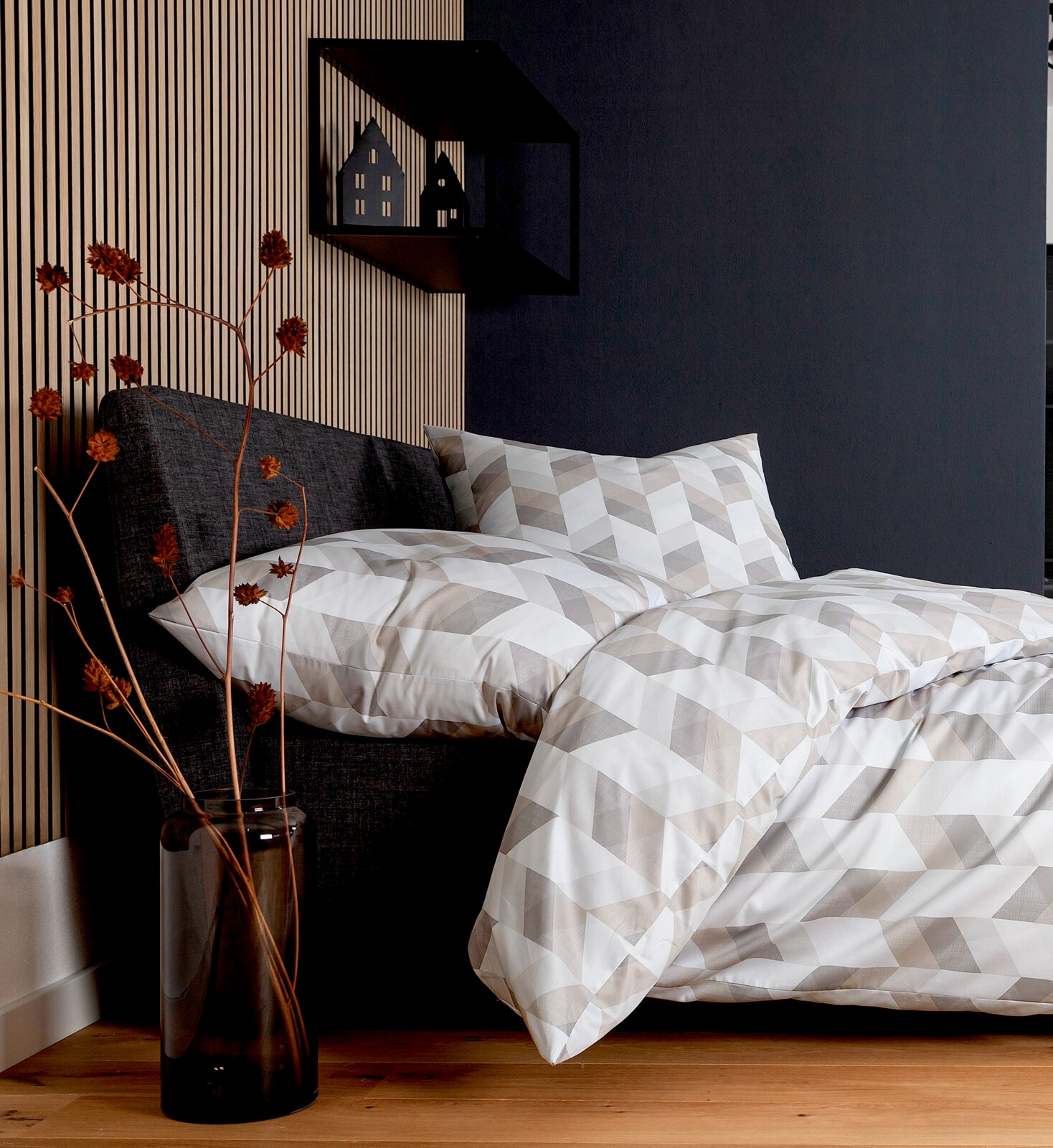 Janine Bettwäsche 155x220cm PALERMO Bettwäsche-Set in geometrischem Muster auf einem grauen Bett, seitliche Perspektive, mit dekorativem Regal und Trockenblumen im Hintergrund.