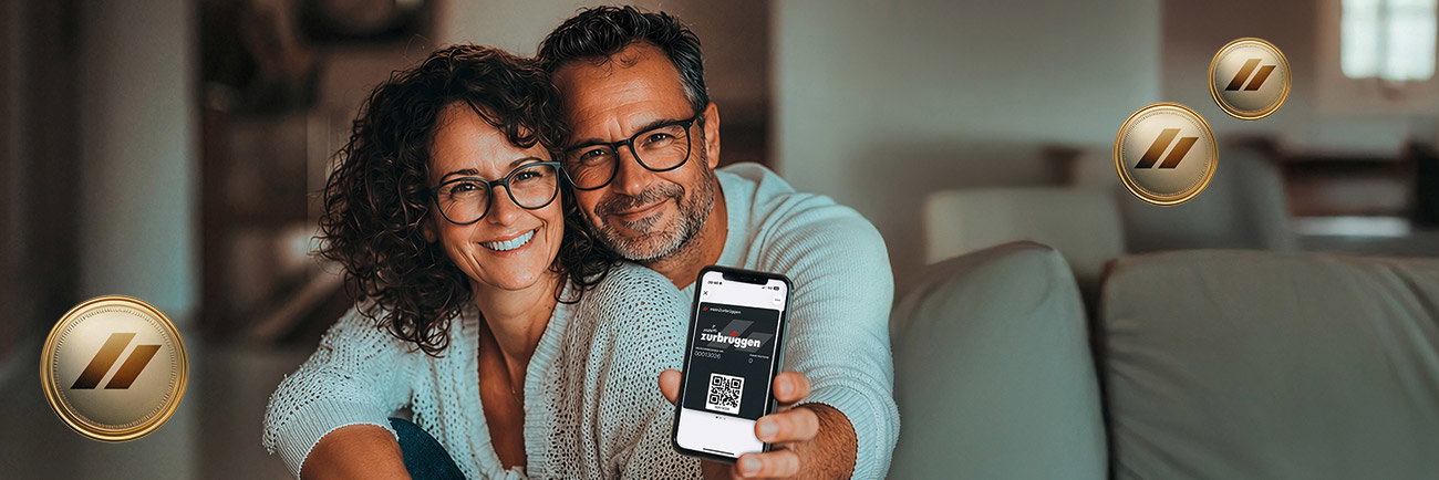 Lächelndes Paar mit Smartphone und Bonusmünzen in gemütlicher Wohnatmosphäre.