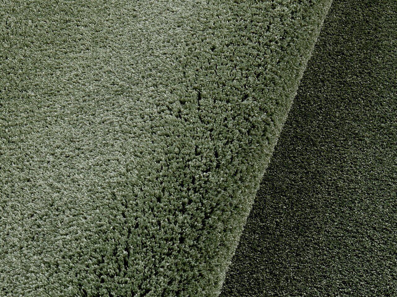 Nahaufnahme eines weichen, runden Teppichs in Grün, perspektivisch von oben fotografiert.