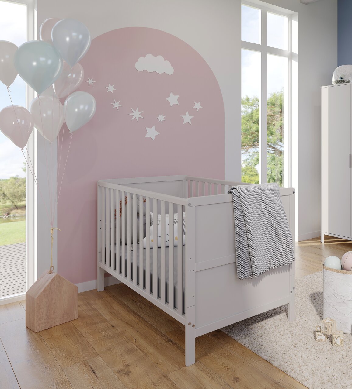 Babyzimmer mit weißem Gitterbett, rosa Wand mit Wolken- und Sternendekoration, Luftballons und Holzboden, seitliche Perspektive