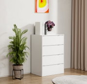 Weiße Kommode mit vier Schubladen in modernem, minimalistischem Design, leicht schräg von vorne rechts fotografiert; oben liegen Bücher und eine Vase mit Hortensien, daneben steht eine grüne Zimmerpflanze im Topf.