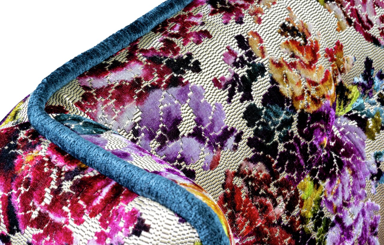 Barnickel Bank FLAIR Nahaufnahme aus schräger Perspektive auf ein dekoratives Kissen mit mehrfarbigem Blumenmuster in Jacquard-Optik und blauem Paspelrand.