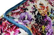 Nahaufnahme aus schräger Perspektive auf ein dekoratives Kissen mit mehrfarbigem Blumenmuster in Jacquard-Optik und blauem Paspelrand.