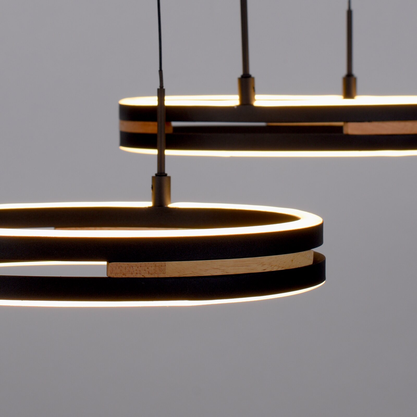 Close-up vanuit zijaanzicht van twee moderne zwarte ronde hanglampen met warmwitte ledverlichting en houten accenten.