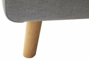 Close-up van een grijs gestoffeerd bed met een houten poot, gezien vanaf de zijkant