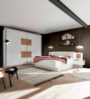 Moderne Schlafzimmeransicht mit weißem Schwebetürenschrank und Bettanlage, seitliche Perspektive