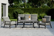Gartenmöbel-Set mit zwei Sesseln, einer Bank und einem Tisch auf einer Terrasse, umgeben von grüner Hecke und Bäumen, aus der Frontperspektive.