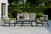Tuinsets met twee fauteuils, een bank en een tafel op een terras, omgeven door een groene haag en bomen, gezien vanuit de voorkant.