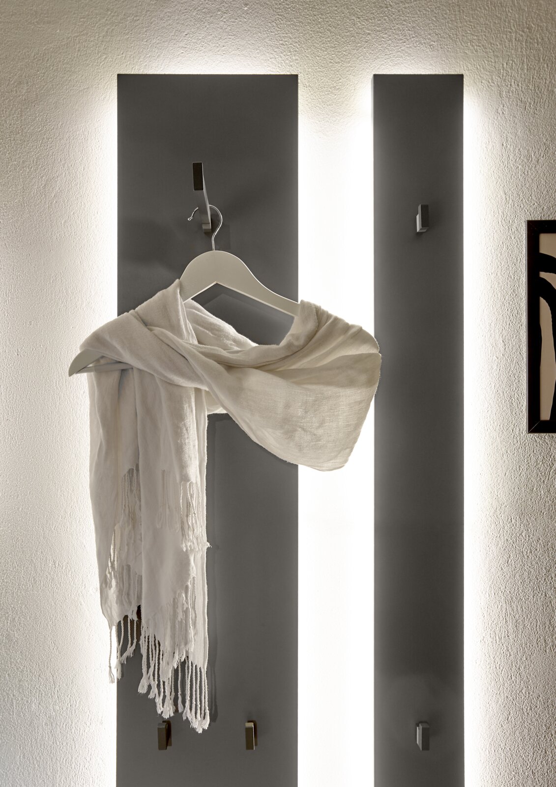 Garderoben-Set mit drei vertikalen Paneelen, beleuchtet von hinten, mit Haken und einem weißen Schal auf einem Kleiderbügel. Frontalansicht.