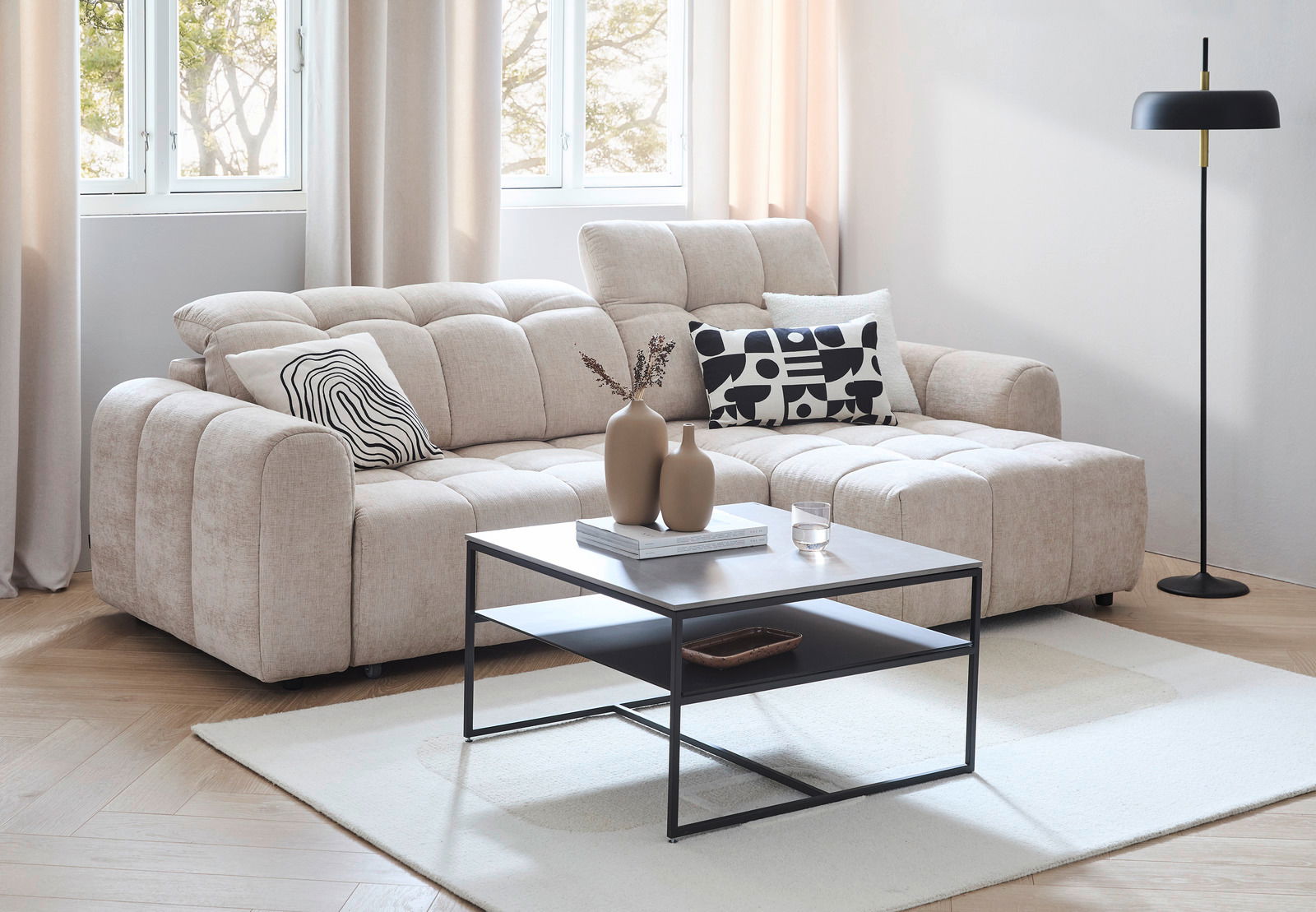 Beige Longchairkombination MARSEILLE in einem modernen Wohnzimmer, mit einem schwarzen Couchtisch und dekorativen Kissen, aus der Perspektive von vorne links.