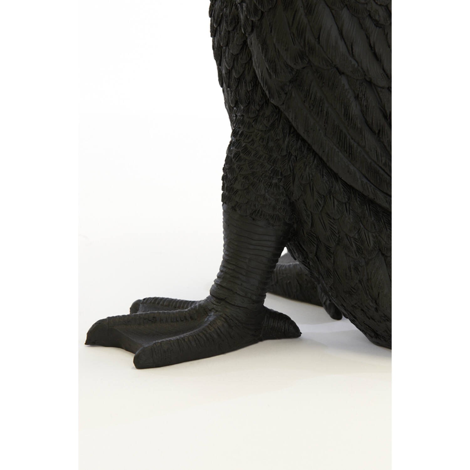 Detailaufnahme aus seitlicher Perspektive: schwarze Vogelfigur/Skulptur mit strukturierter Federoberfläche und großen, kräftigen Füßen vor weißem Hintergrund