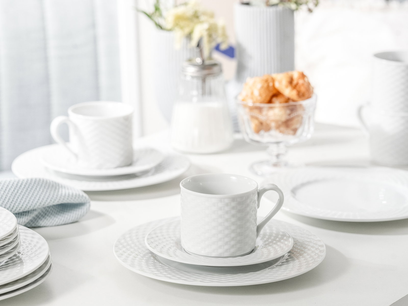 Weißes Kaffeeservice mit Tassen und Tellern in eleganter Textur, seitliche Perspektive auf einem gedeckten Tisch.