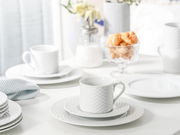 Weißes Kaffeeservice mit Tassen und Tellern in eleganter Textur, seitliche Perspektive auf einem gedeckten Tisch.