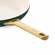 Nahaufnahme einer Pfanne mit goldfarbenem Griff und cremefarbener Innenbeschichtung, seitliche Perspektive