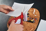 Rote Vielzweckschere schneidet ein Blatt Papier, seitliche Perspektive