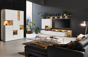 Moderne Wohnzimmeransicht mit der Vitrine Venjakob ANDIAMO HOME in Weiß, beleuchteten Fächern und stilvoller Dekoration, seitliche Perspektive.