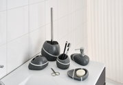 Badkamerset van grijze steen met witte strepen, bestaande uit een zeepdispenser, tandenborstelhouder, beker, zeepbakje en toiletborstelhouder, gefotografeerd vanaf de voorkant op een witte wastafel.