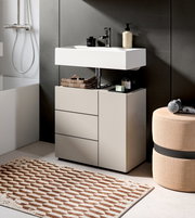 Modernes Badezimmer-Waschtisch-Set mit weißem Aufsatzwaschbecken, Armatur und Unterschrank mit Schubladen vor grauer Wand, perspektivisch in leicht schräger Frontansicht.