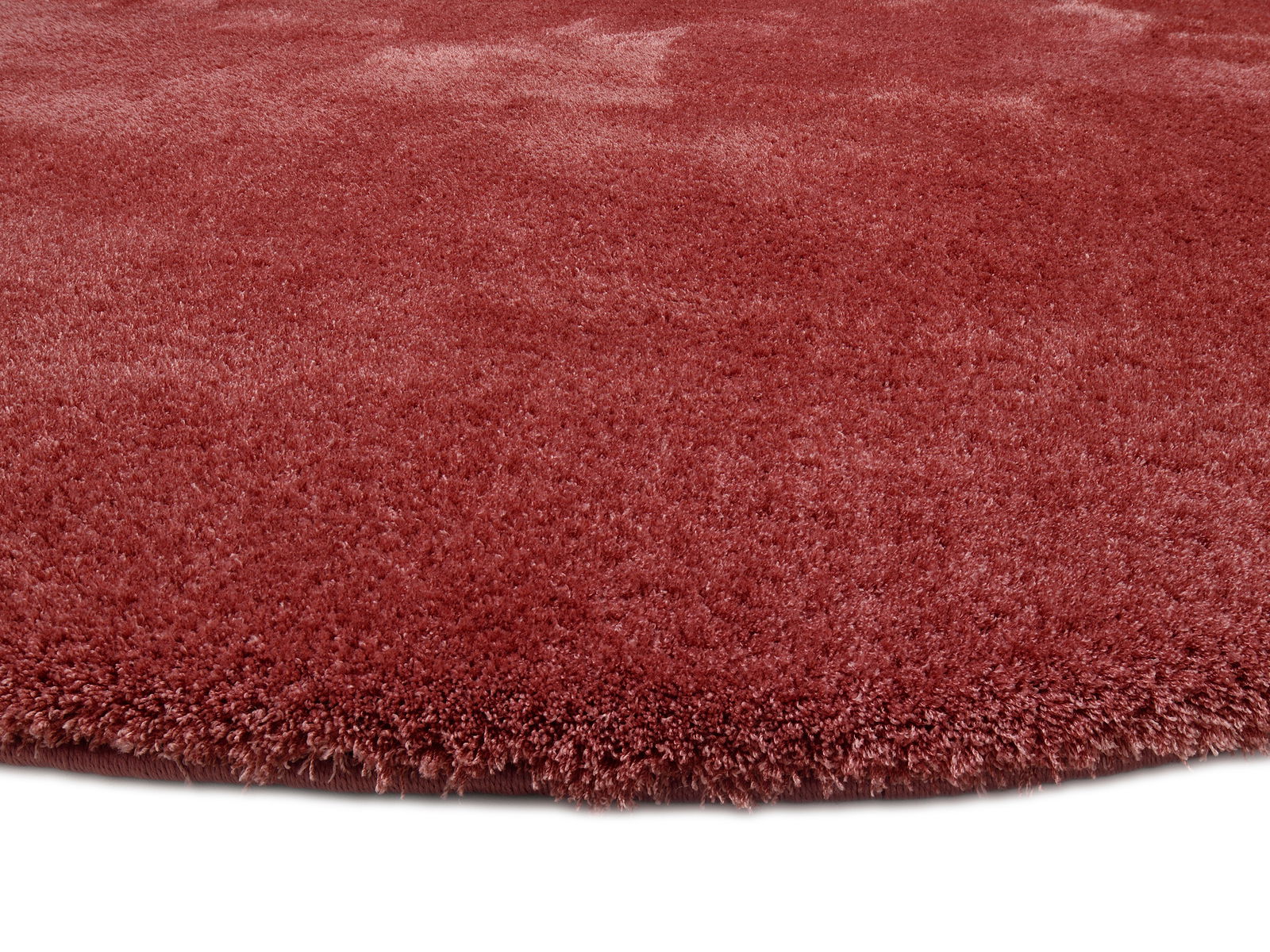 Runder, weicher Teppich in Rot aus der Nähe fotografiert, zeigt die flauschige Textur.