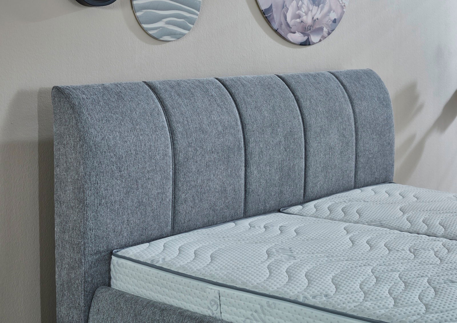 Graues Polsterbettgestell mit gestepptem Kopfteil, seitliche Perspektive