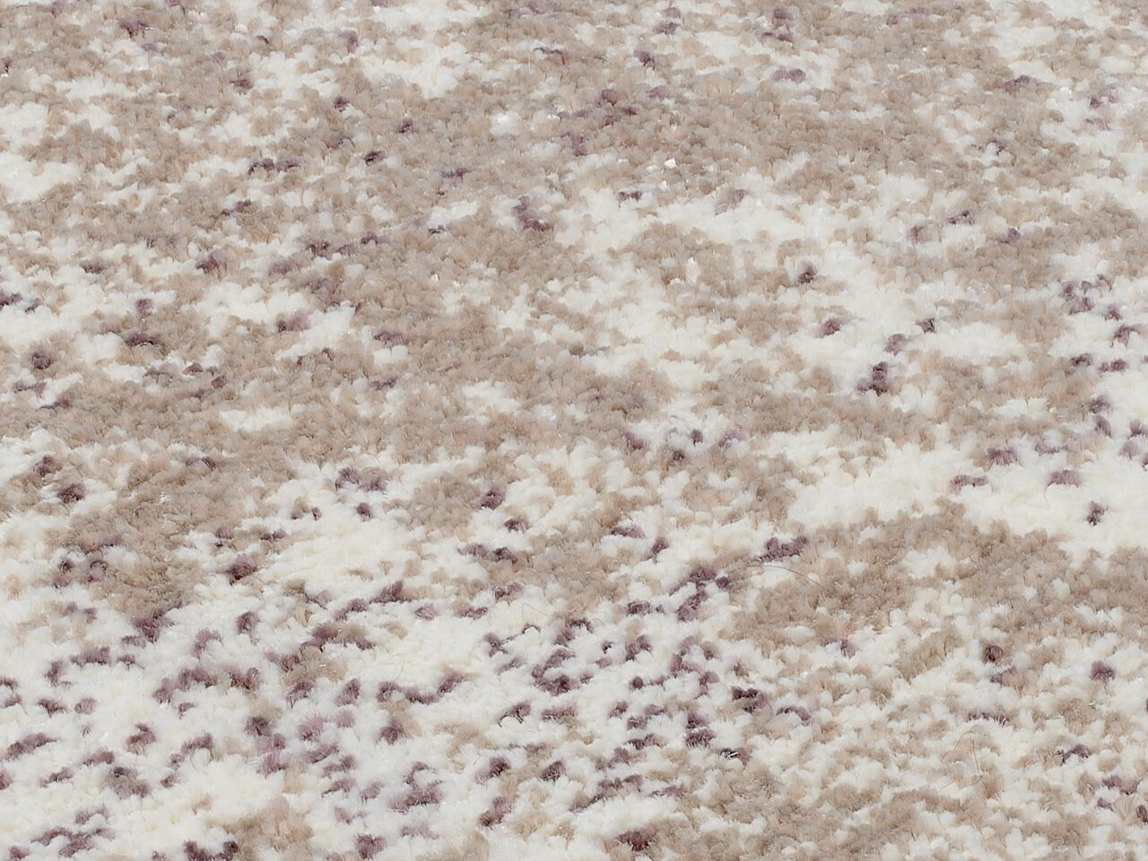 Nahaufnahme eines Designer Teppichs mit beigem und weißem Muster, aus seitlicher Perspektive fotografiert.