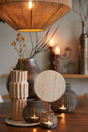 Stimmungsvolle Wohnzimmerszene mit hängender Lampe, dekorativen Vasen und Kerzenhaltern auf einem Holztisch, aus der Perspektive von vorne.