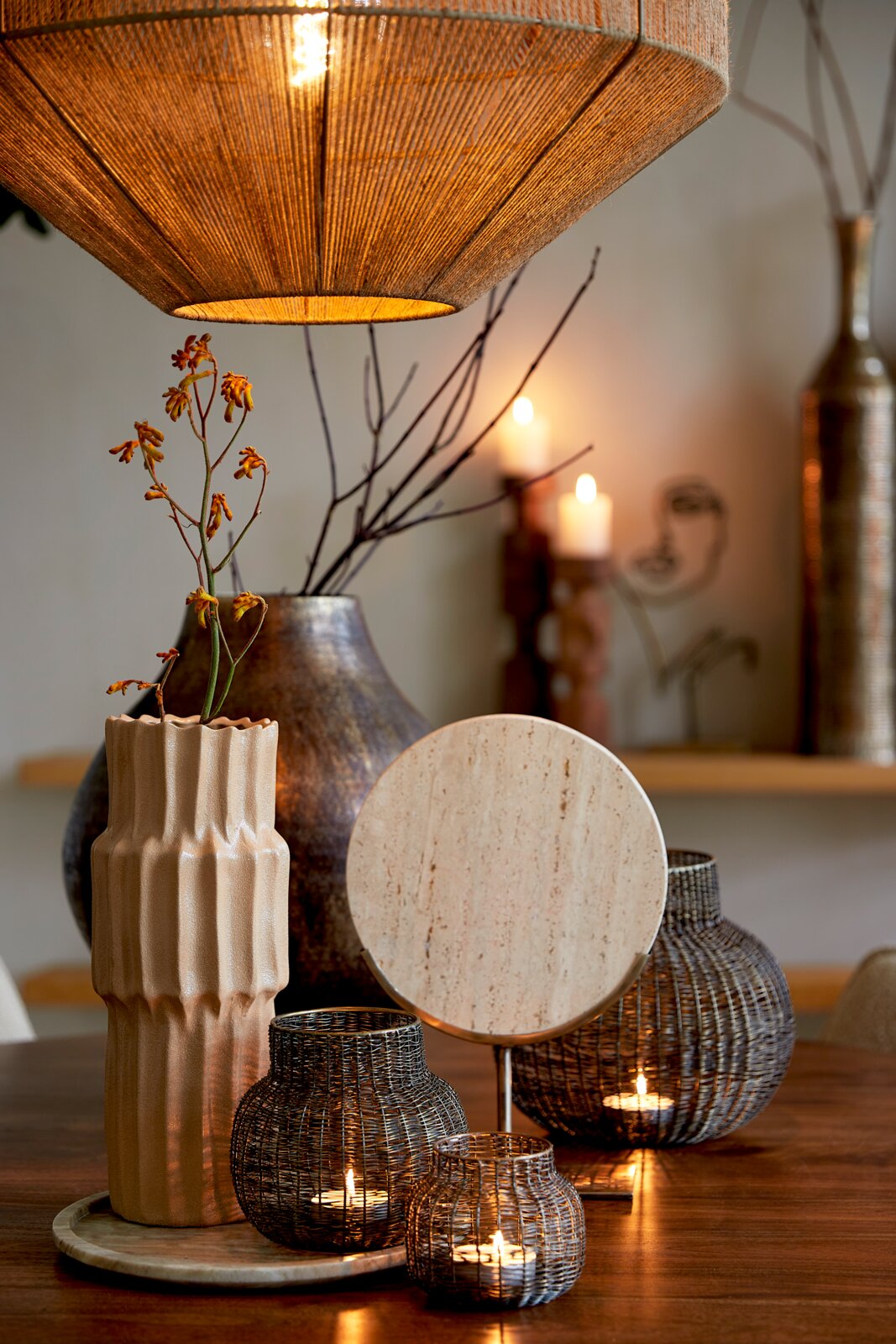 Sfeervolle woonkamerscène met een hanglamp, decoratieve vazen en kandelaars op een houten tafel, gezien vanuit het vooraanzicht.
