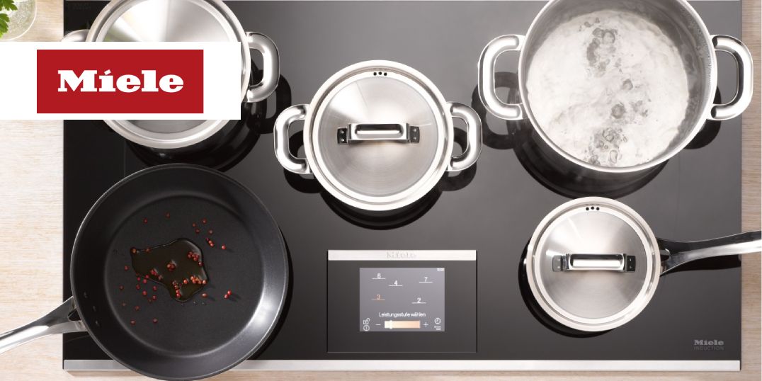 Ein Miele Induktionskochfeld mit einer Bratpfanne und drei Edelstahltöpfen.