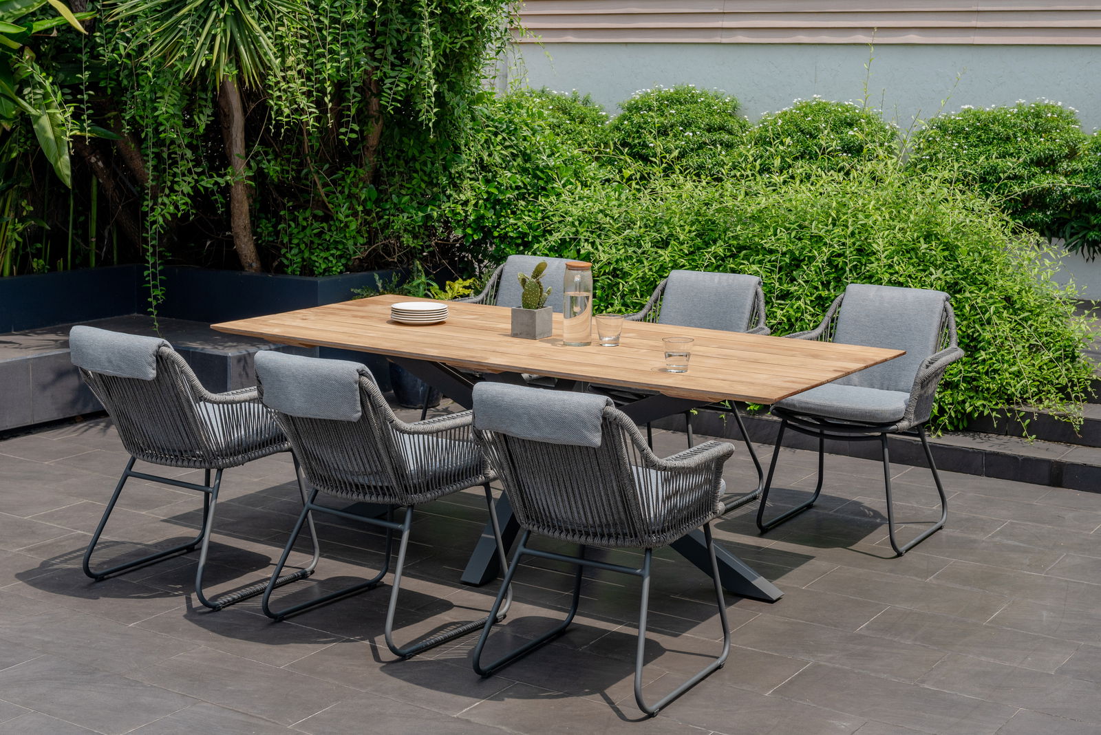 Amatio Armlehnstuhl CIRCLE Moderner Armlehnstuhl aus grauem Geflecht und Metallgestell, Teil einer stilvollen Outdoor-Essgruppe mit Holztisch, seitliche Perspektive.