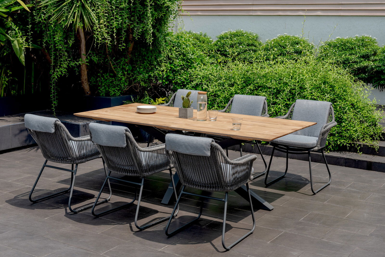 Amatio Armlehnstuhl CIRCLE Moderner Armlehnstuhl aus grauem Geflecht und Metallgestell, Teil einer stilvollen Outdoor-Essgruppe mit Holztisch, seitliche Perspektive.