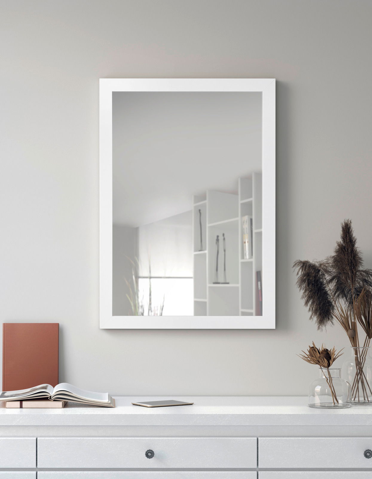 Rechteckiger Spiegel mit weißem Rahmen, an einer grauen Wand hängend, mit einer Kommode im Vordergrund. Perspektive: Frontalansicht.