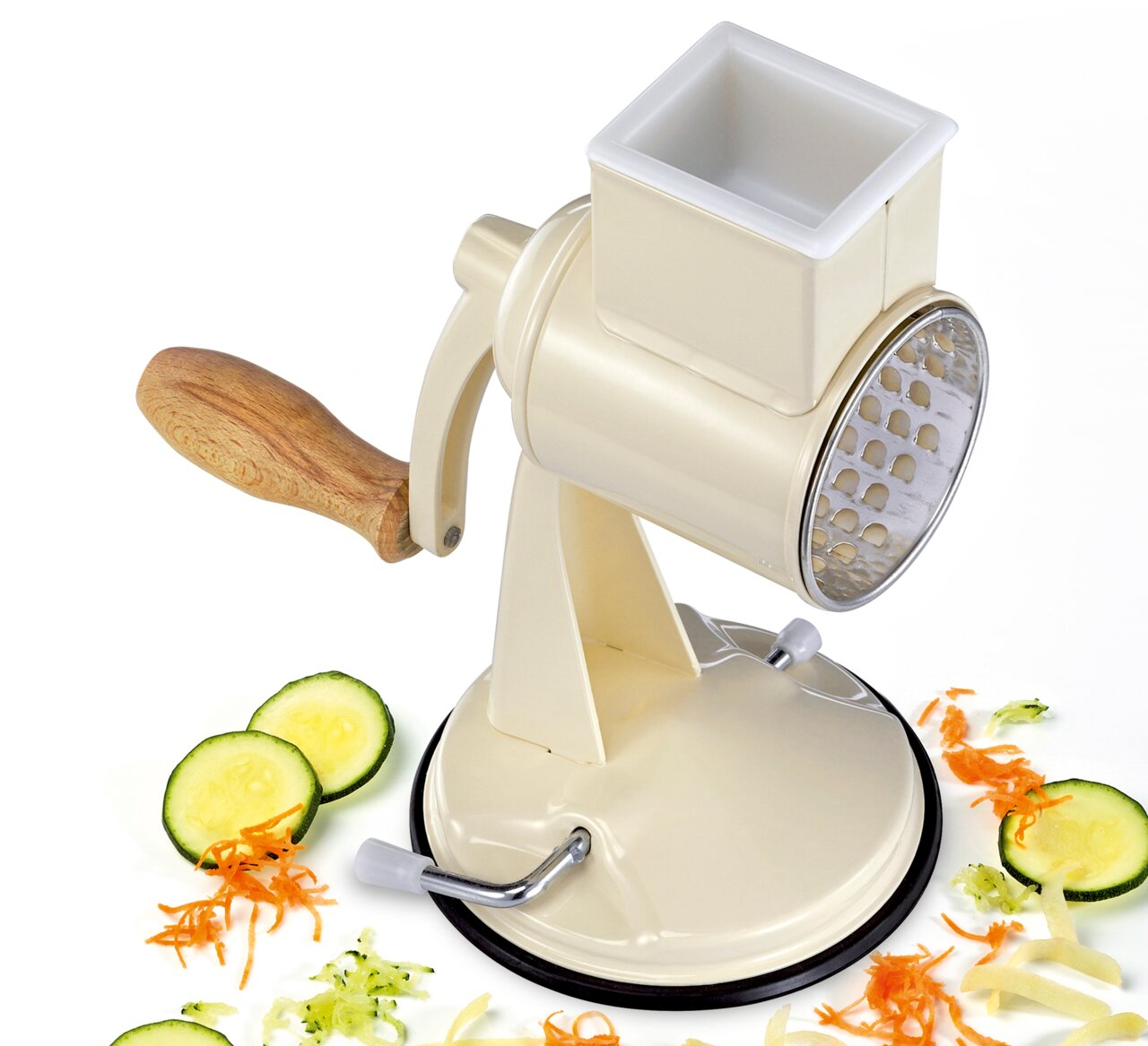 Trommelreibe CLASSIC in creme mit Holzgriff, seitliche Perspektive, umgeben von geriebenem Gemüse wie Gurken und Karotten.