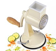 Trommelreibe CLASSIC in creme mit Holzgriff, seitliche Perspektive, umgeben von geriebenem Gemüse wie Gurken und Karotten.