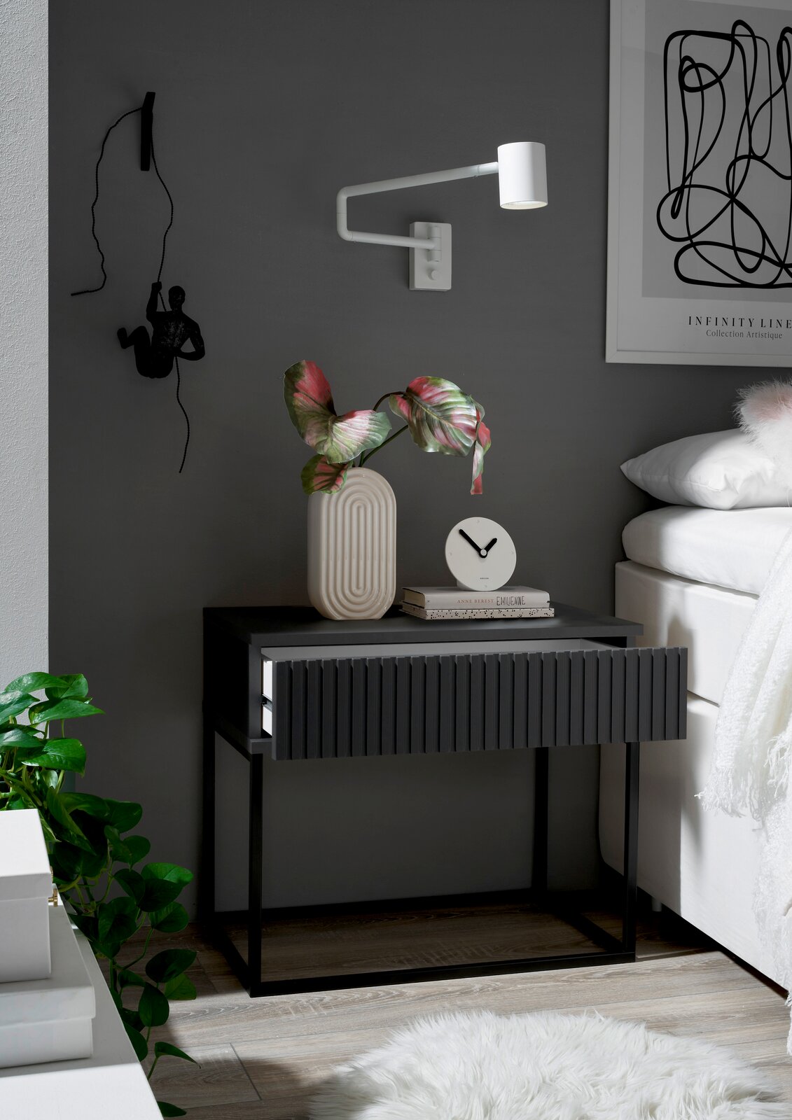 Moderne Nachtkommode in dunklem Grau mit geriffelter Front, dekoriert mit einer Vase und einer Uhr, seitliche Perspektive