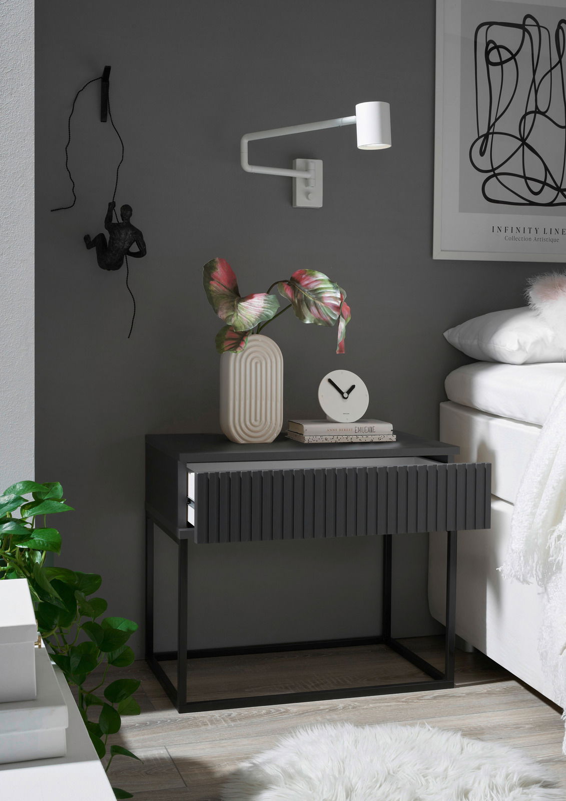 Moderne Nachtkommode in dunklem Grau mit geriffelter Front, dekoriert mit einer Vase und einer Uhr, seitliche Perspektive