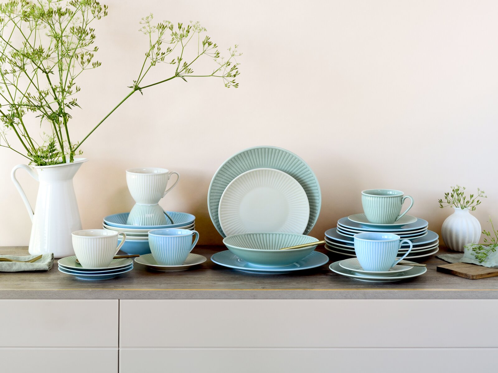 Creatable Kombiservice 30-tlg VALENCIA Pastellfarbenes, geriffeltes Keramik-Geschirrset in Weiß, Mint und Hellblau mit Tellern, Schalen und Tassen auf Holztisch, dekoriert mit Vasen und Grünzweigen, frontal aus leicht erhöhter Perspektive