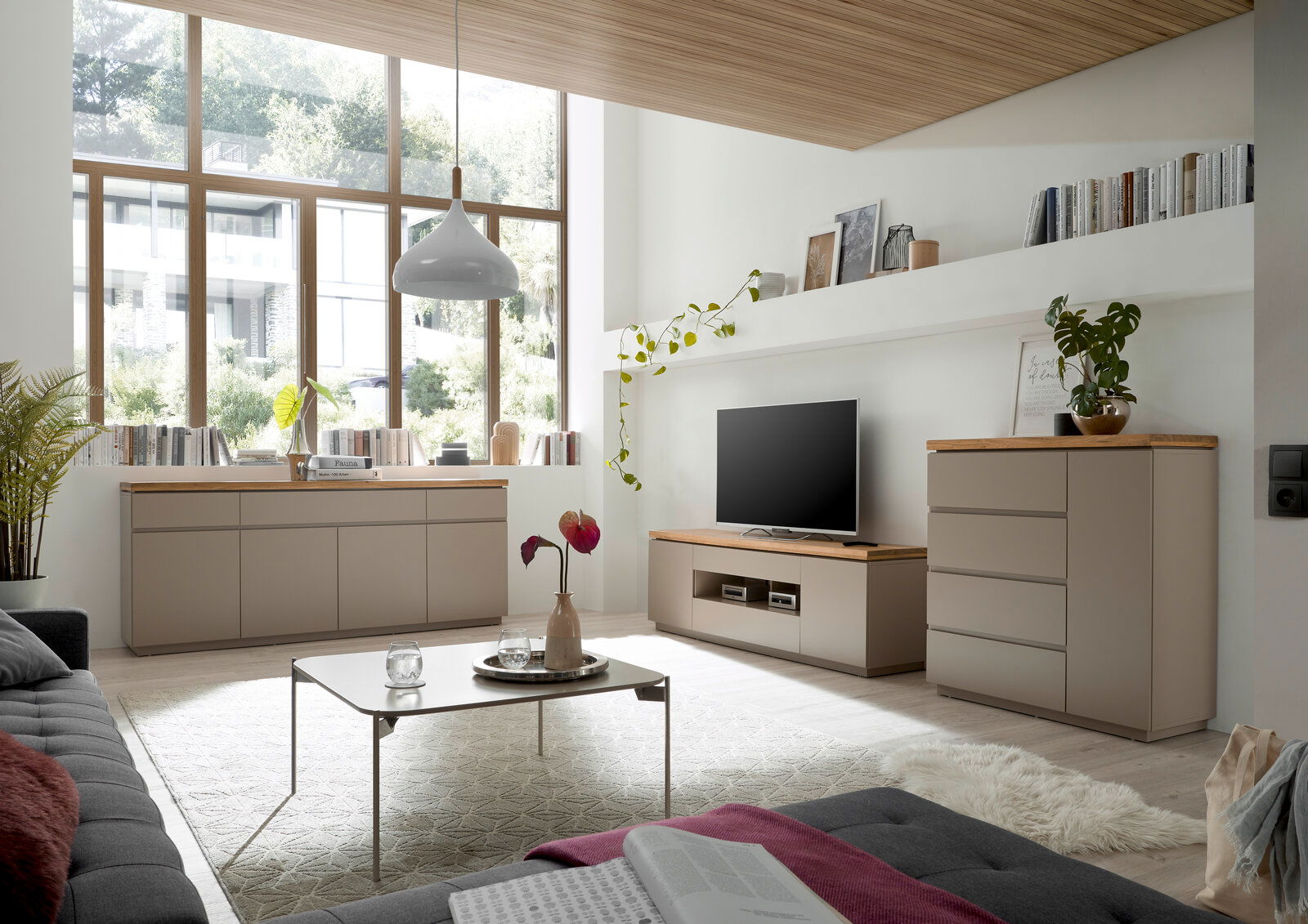 Modernes Wohnzimmer mit TV-Lowboard, Sideboard und Kommode in hellem Holz und neutralen Farben, seitliche Perspektive