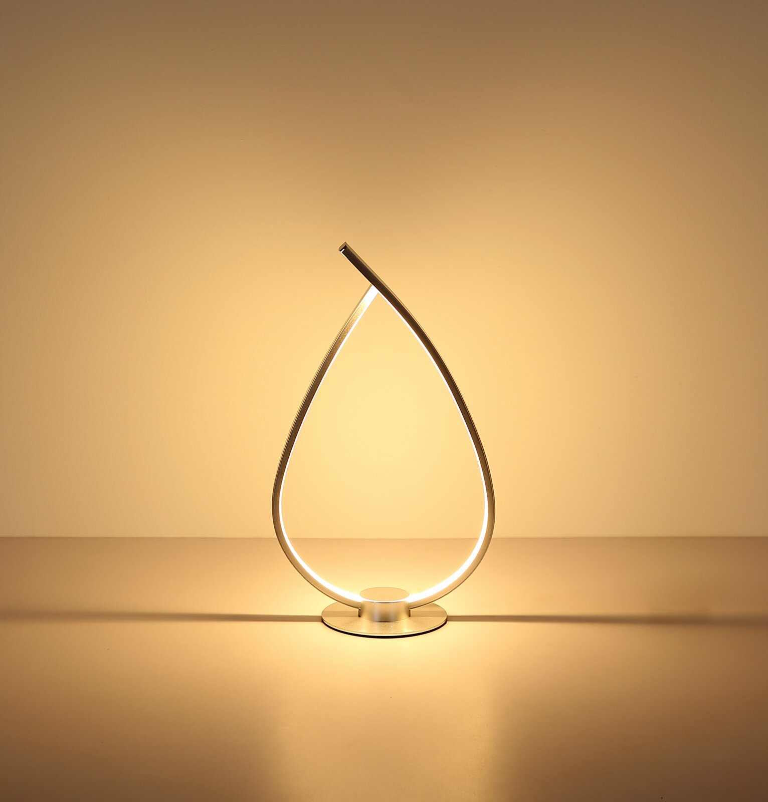 Moderne LED-Tischleuchte in tropfenförmigem, gebogenem Design aus silberfarbenem Metall mit warmweißem Licht auf runder Basis, frontal auf Augenhöhe fotografiert