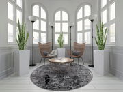 Runder Designer Teppich in einem eleganten Raum mit großen Fenstern, modernen Stühlen und Pflanzen, aus der Perspektive von oben betrachtet.