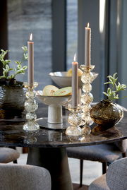 Elegante Kerzenhalter aus Glas mit glitzernden Details, auf einem stilvoll gedeckten Tisch mit modernen Dekorationen. Perspektive: seitlich von vorne.