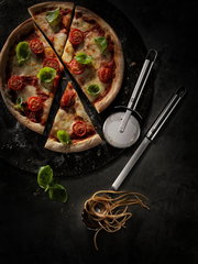 Pizzaschneider Pro neben einer frisch gebackenen Pizza mit Tomaten und Basilikum, von oben betrachtet.
