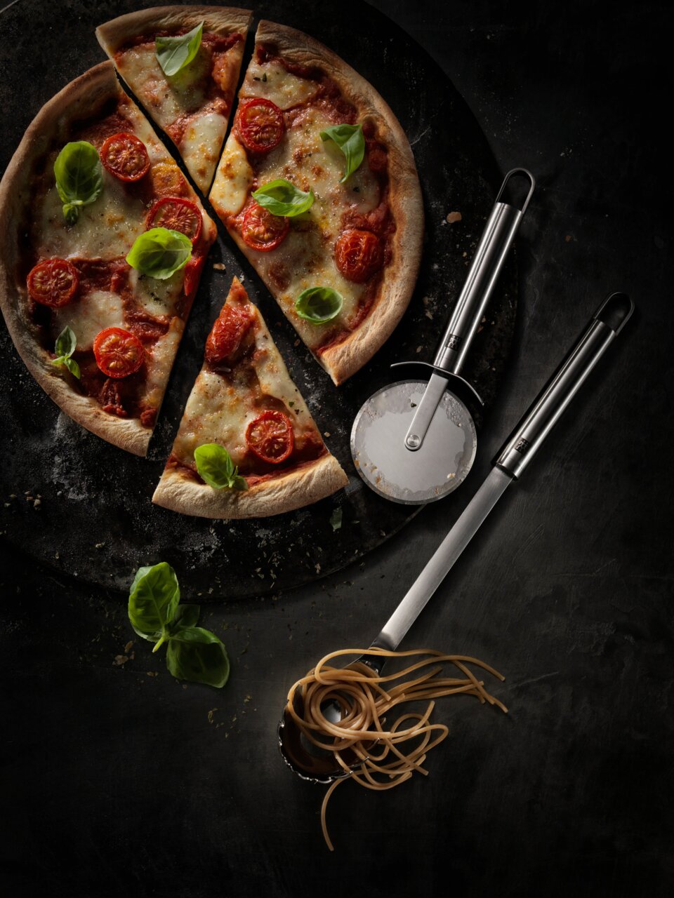Pizzaschneider Pro neben einer frisch gebackenen Pizza mit Tomaten und Basilikum, von oben betrachtet.