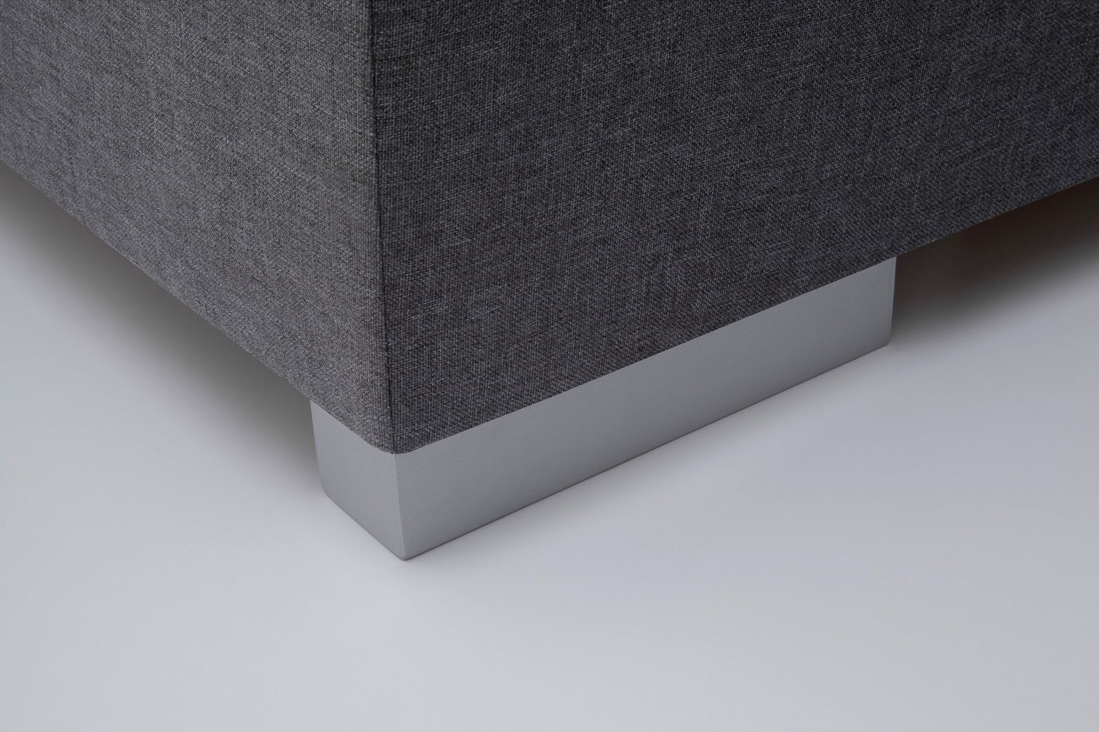 Nahaufnahme der Ecke eines Boxbetts mit grauem Stoffbezug und silbernem Fuß, Perspektive von unten.