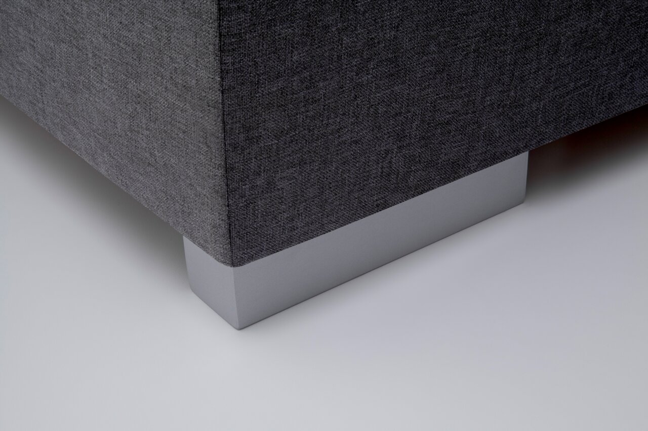 Close-up van de hoek van een boxspring met grijze stoffen bekleding en een zilveren voet, gezien van onderaf.