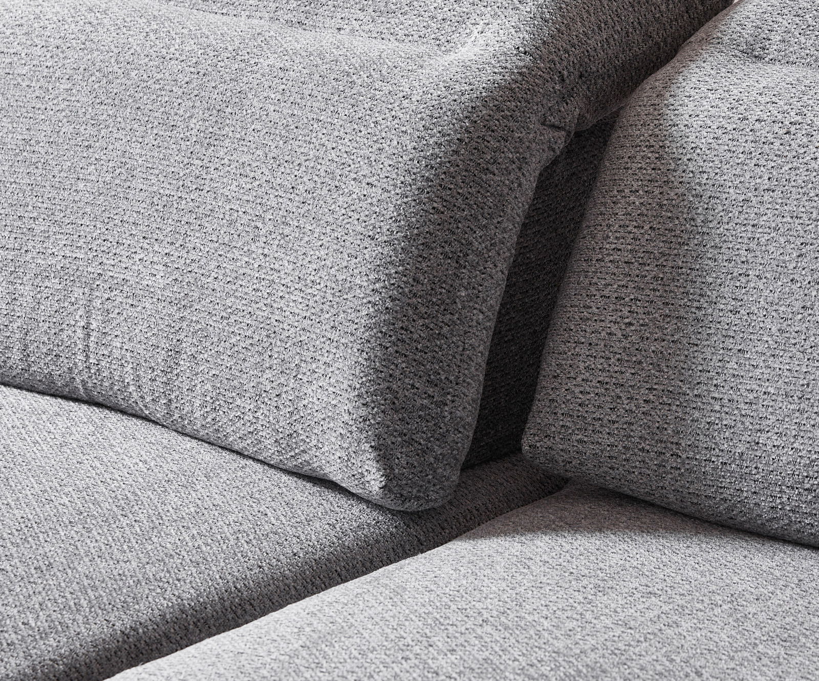 Nahaufnahme einer grauen Longchairkombination mit strukturierter Stoffoberfläche, seitliche Perspektive.