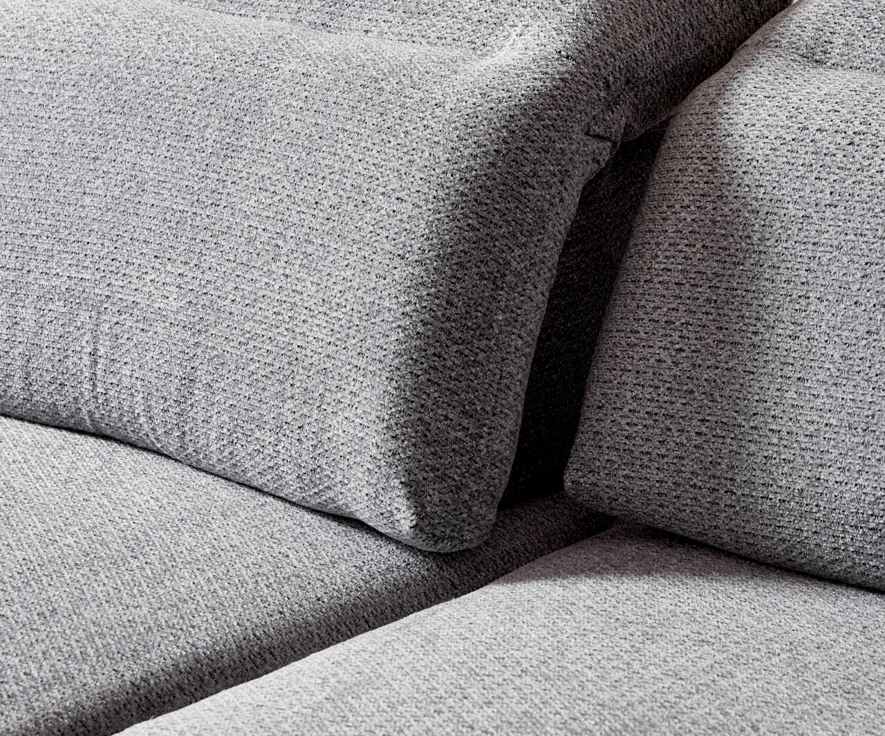 Close-up van een grijze longchair-set met een gestructureerd stoffen oppervlak, gezien vanaf de zijkant.