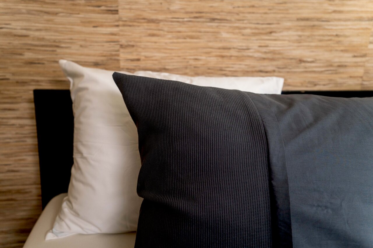 Nahaufnahme von Bettwäsche in dunklem Grau und Weiß auf einem Bett mit Holzrückwand.