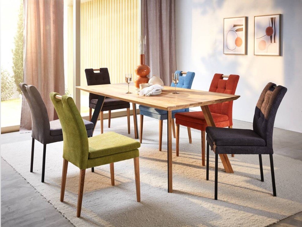 Esszimmer mit einem Holztisch und sechs bunten Stühlen der Serie BARCELONA, Perspektive von schräg vorne.