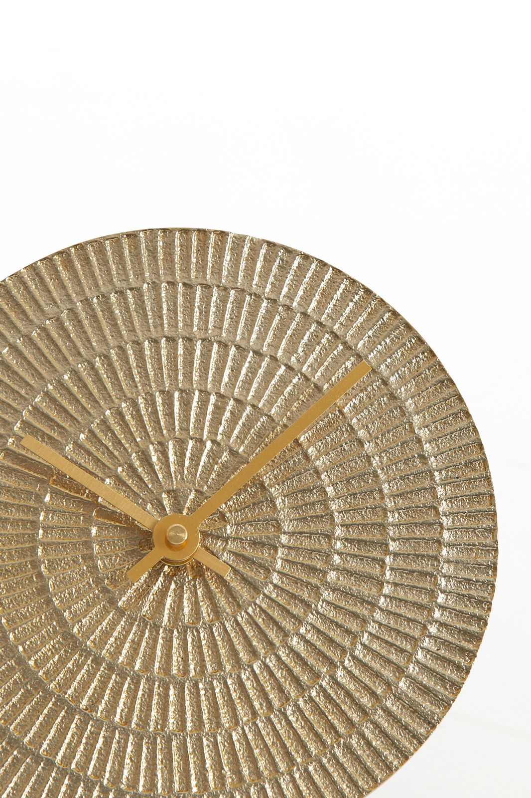 Nahaufnahme einer runden, hell goldenen Uhr mit strukturiertem Zifferblatt und goldenen Zeigern, von vorne betrachtet.